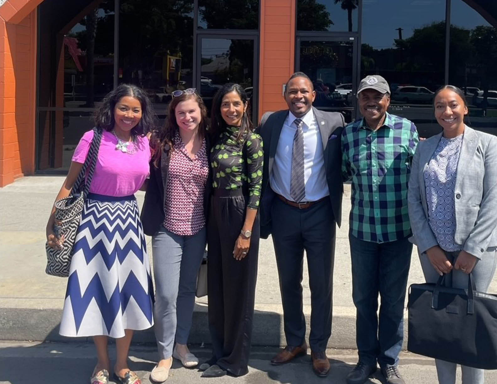 Five people pose in front of a building, two men and three women. They are all wearing ties, with one man wearing a suit. The building is the Los Angeles Sentinal. AI generated content