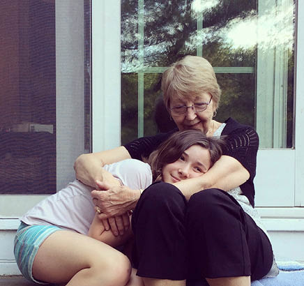 Playful portrait of a grandmother hugging and cuddling her pre-teen granddaughter as they sit on patio steps at home. Elderly woman wraps her arms around her granddaughter with love and affection. Childhood. Friendship. Family.